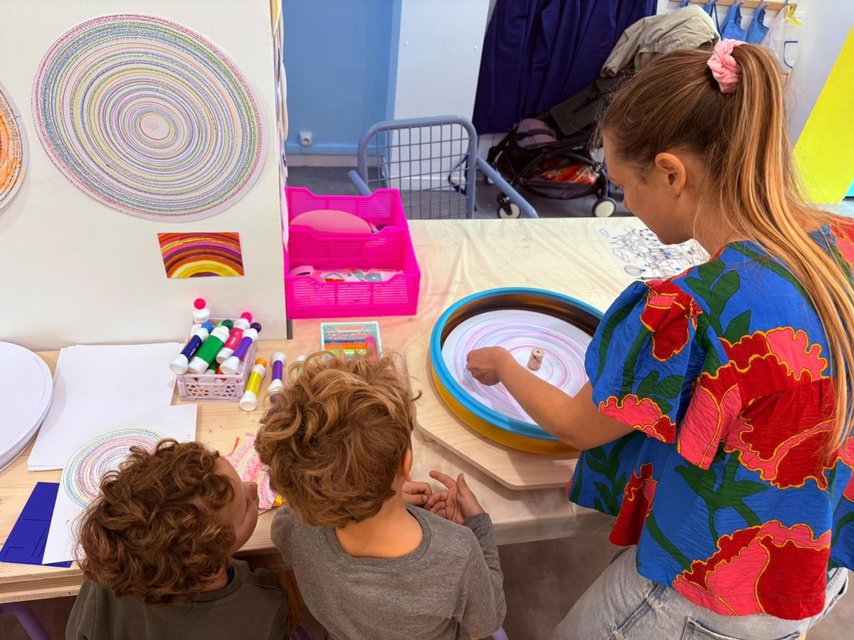 Deux enfants regardent tourner la machine à spin-art, leurs créations circulaires affichées au mur