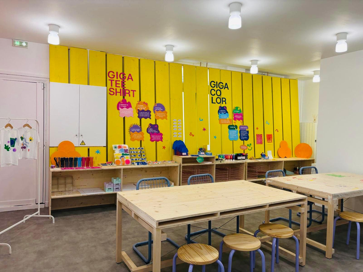 L'espace atelier de GIGACOLOR avec le mur jaune GIGA TEE SHIRT et ses modèles de tee-shirts