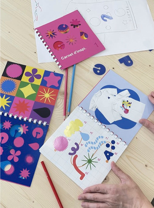 Le carnet d’inspiration GIGACOLOR ouvert sur la table d’atelier, crayons et pochoirs autour